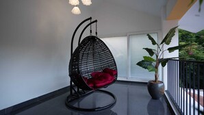 Ein schwarzer, gewebter Stuhl mit rotem Kissen auf einem Balkon mit Topfpflanze und Geländer.