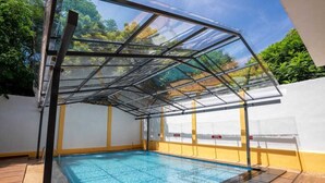 Une piscine dotée d’une enceinte en verre, entourée d’un mur blanc et jaune, et agrémentée d’une terrasse en bois.