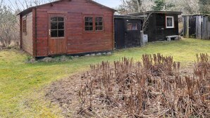 A rustic wooden cabin with a small attached shed, surrounded by a grassy area and sparse vegetation. - 5 Star Holiday Home in Vig (Vig)