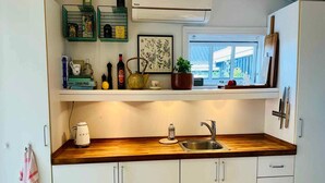 Een keuken met witte kastjes, een houten aanrecht, een spoelbak en een raam met uitzicht op groen.
