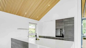 A modern kitchen with a large island, white bar stools, and a wooden ceiling. - 5 Star Holiday Home in Sunds (Sunds)