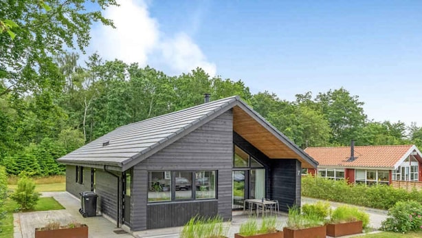 A modern house with a sloped roof, large windows, and a small patio area with outdoor seating. - 5 Star Holiday Home in Sunds (Sunds)