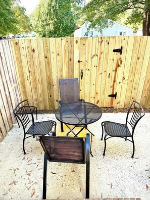 Eine Terrasse mit einem runden Metalltisch und vier Stühlen, umgeben von einem Holzzaun.
