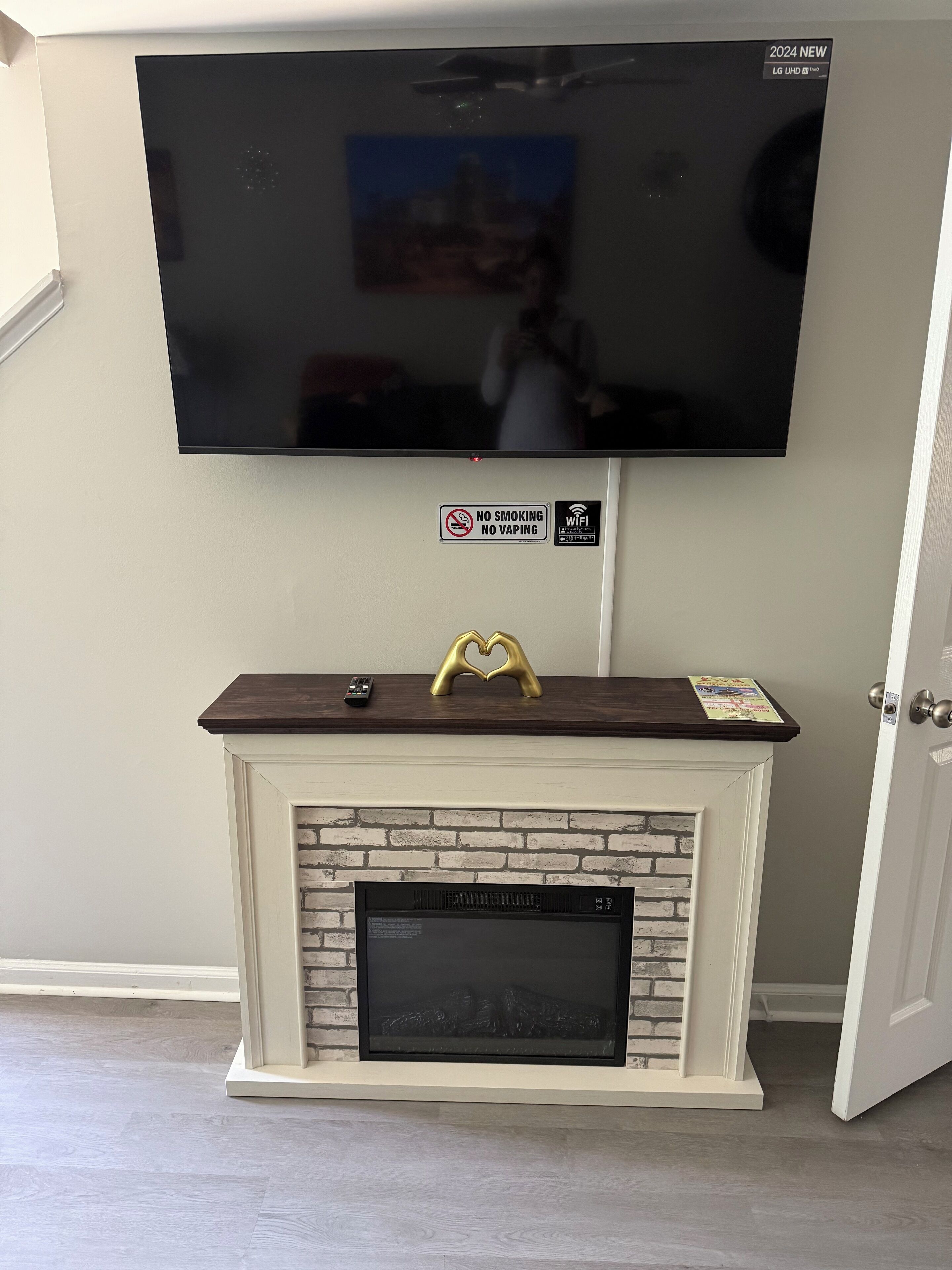 Un televisor de pantalla plana montado en la pared sobre una chimenea, con un cartel de no fumar y no vapear, y un símbolo de Wi-Fi.