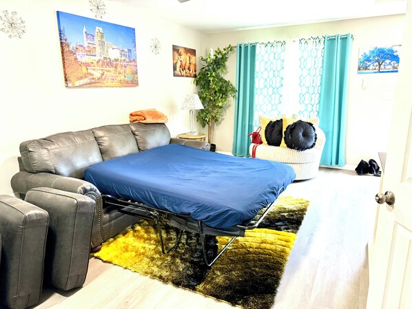 A bedroom with a bed, a sofa, a small table, and a potted plant.