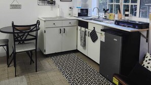A compact kitchen with white cabinets, a microwave, a sink, and a window. There are wall decorations and a patterned rug.