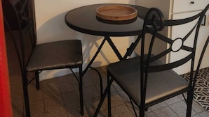 A small dining area with a round table and two chairs, a kitchen counter with a wire rack, and three wall-mounted signs with humorous messages.