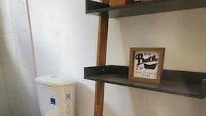 A bathroom with a toilet, a shelf with a sign, and a wooden bucket.