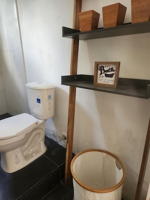 A bathroom with a toilet, a shelf with a sign, and a wooden bucket.