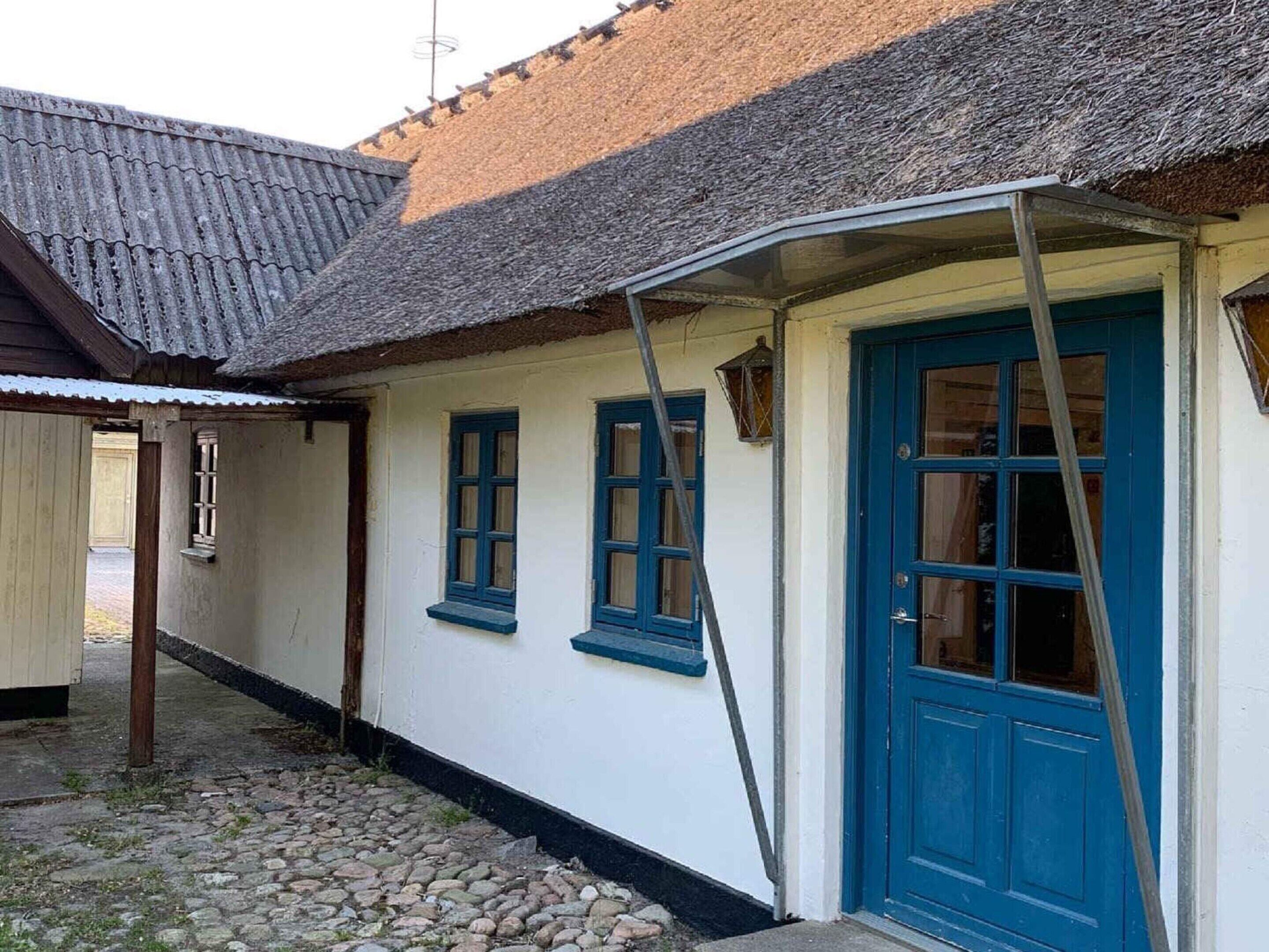 Une maison traditionnelle avec un toit de chaume, une porte bleue et des murs blancs.
