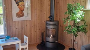 A cozy room with a wood-burning stove, a white table with chairs, and a potted plant. - 5 Star Holiday Home in Ebeltoft (Ebeltoft)