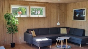 A modern living room with a grey sectional sofa, a small round table, a potted plant, and wooden flooring. - 5 Star Holiday Home in Ebeltoft (Ebeltoft)
