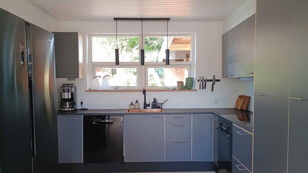 A modern kitchen with grey cabinets, a built-in dishwasher, a coffee maker, and a window with a view of greenery. - 5 Star Holiday Home in Albaek (Aalbaek)