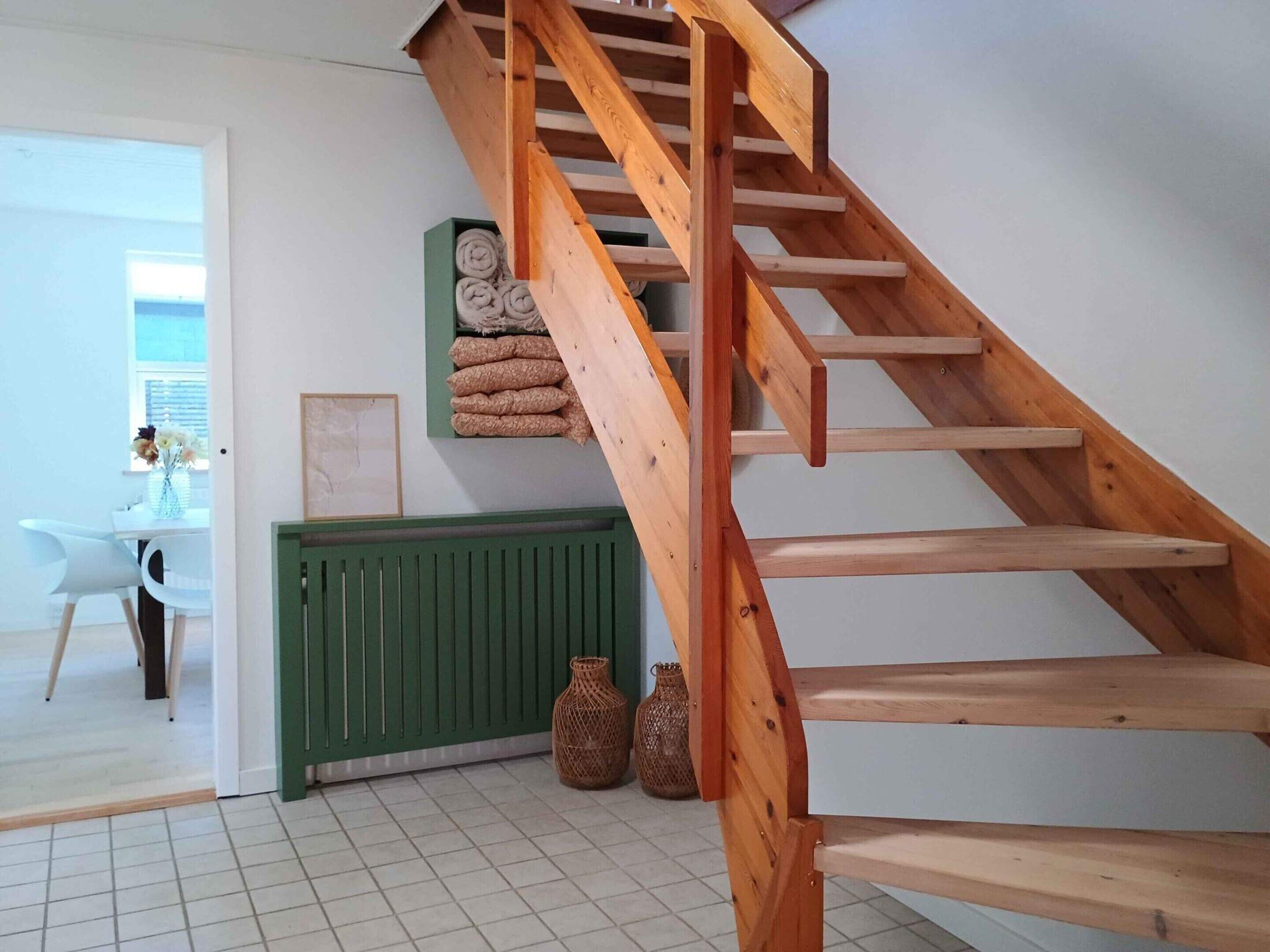 A wooden staircase in a room with a tiled floor, a radiator, and a table with chairs.