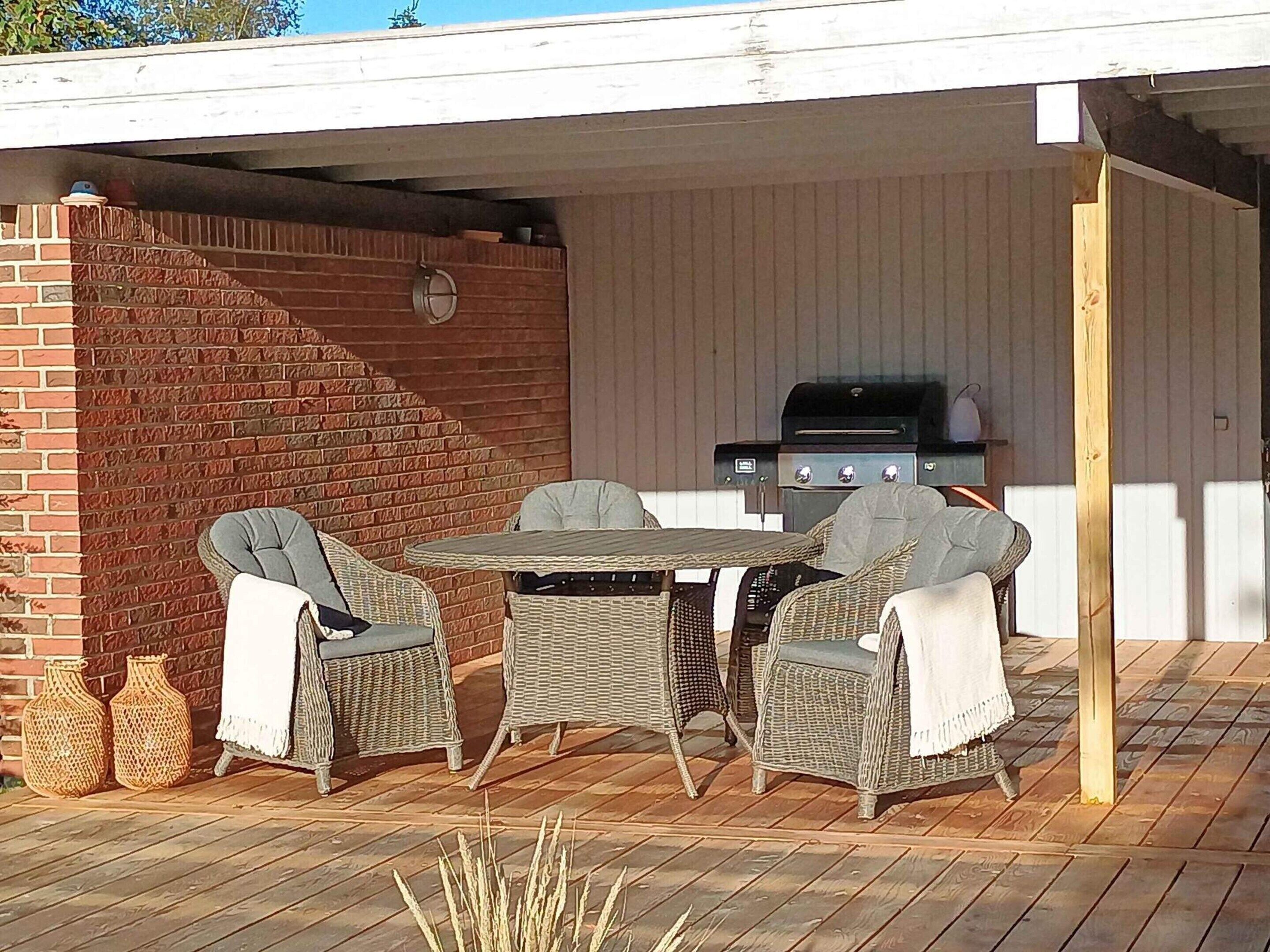 An outdoor patio with wicker furniture, a brick wall, and a grill.