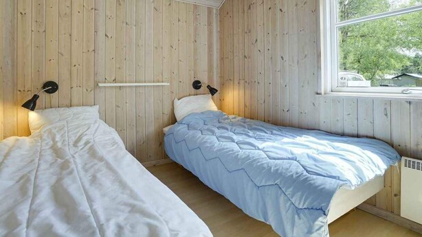 Ein Zimmer mit zwei Betten, Holzwänden, einem Fenster und einer Heizung.