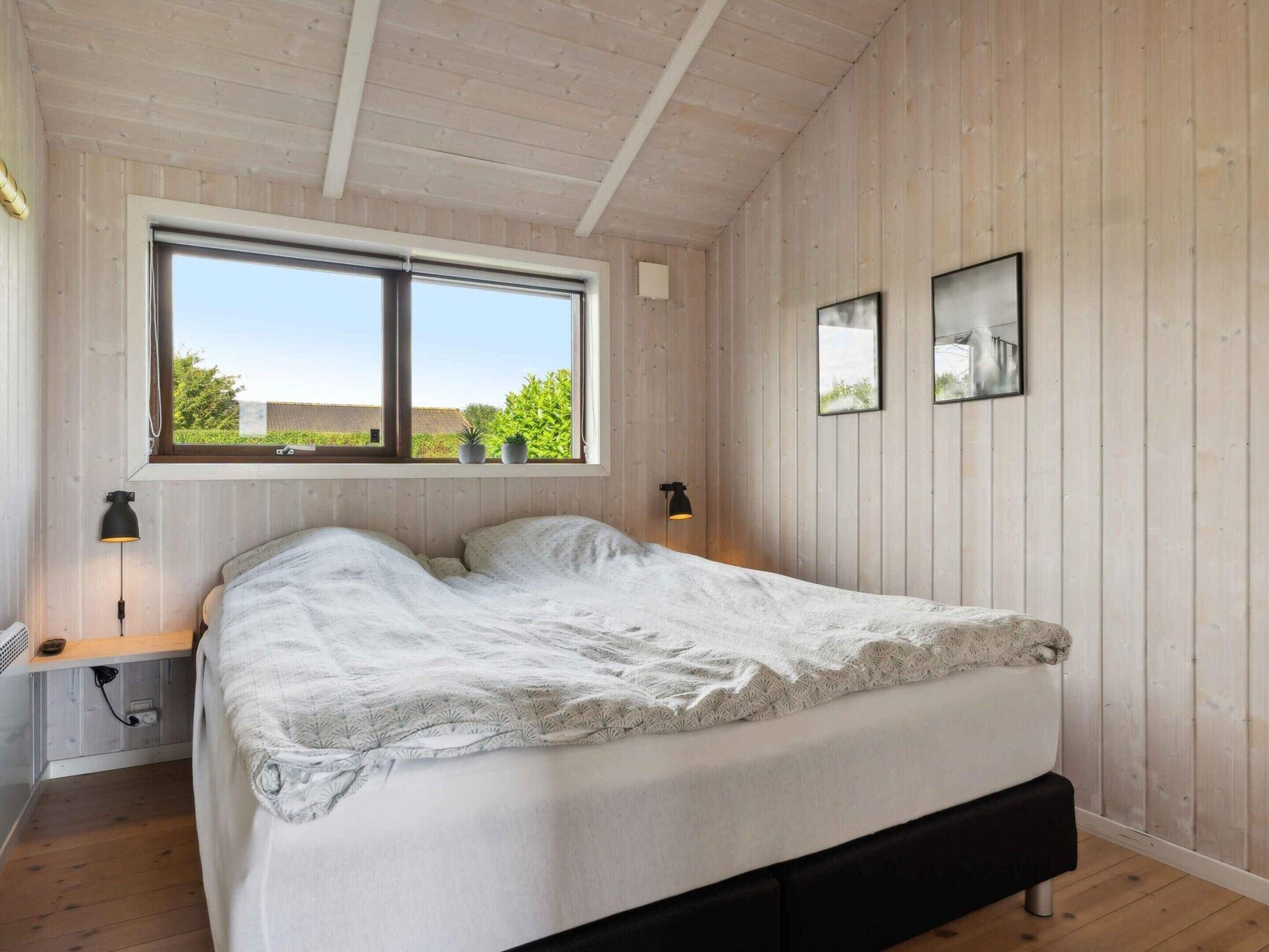 Un dormitorio con un ventanal grande, una cama, dos lámparas de noche y dos cuadros en la pared.