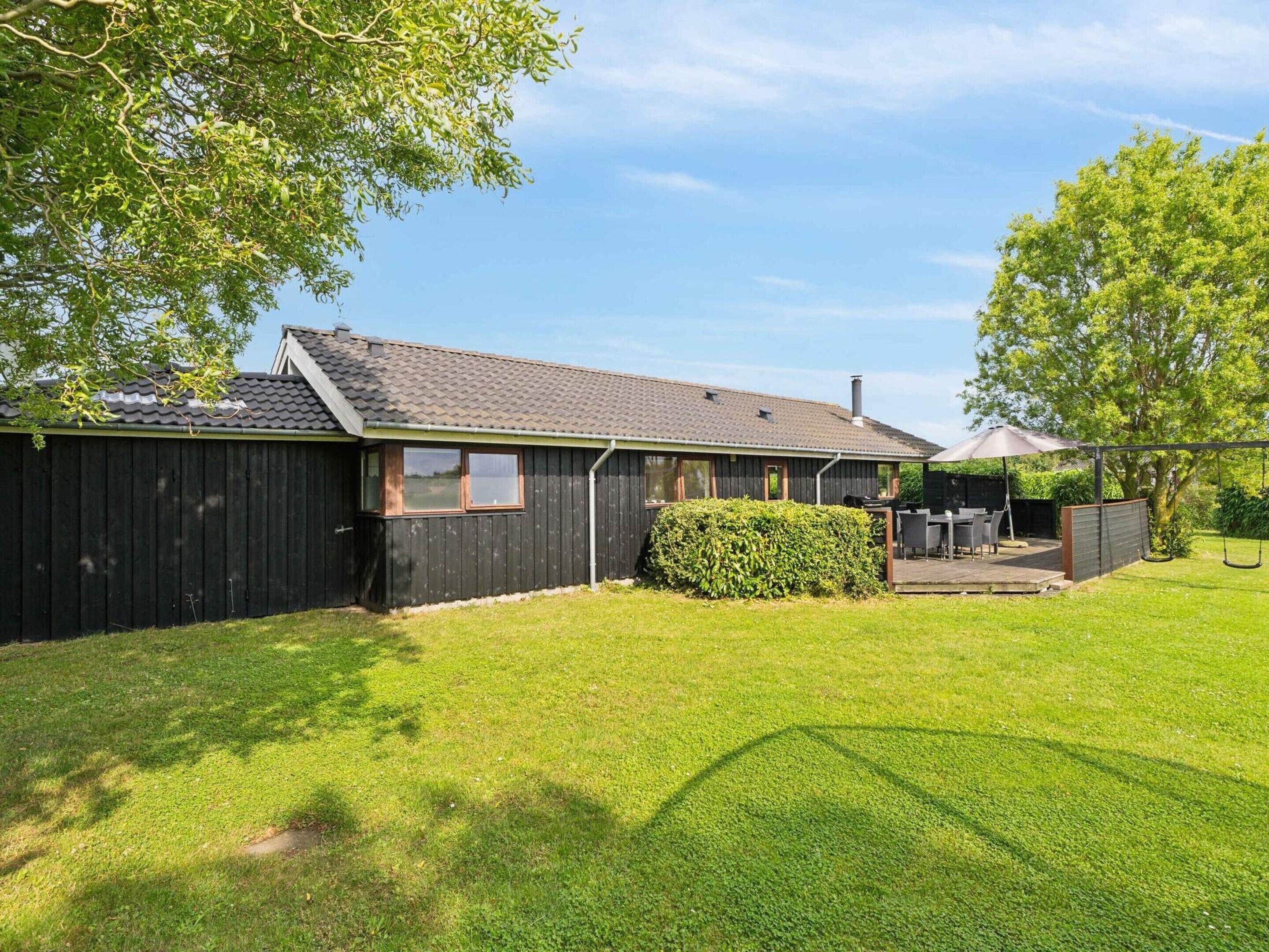 A single-story house with a dark exterior, a tiled roof, and a small deck area with outdoor furniture.