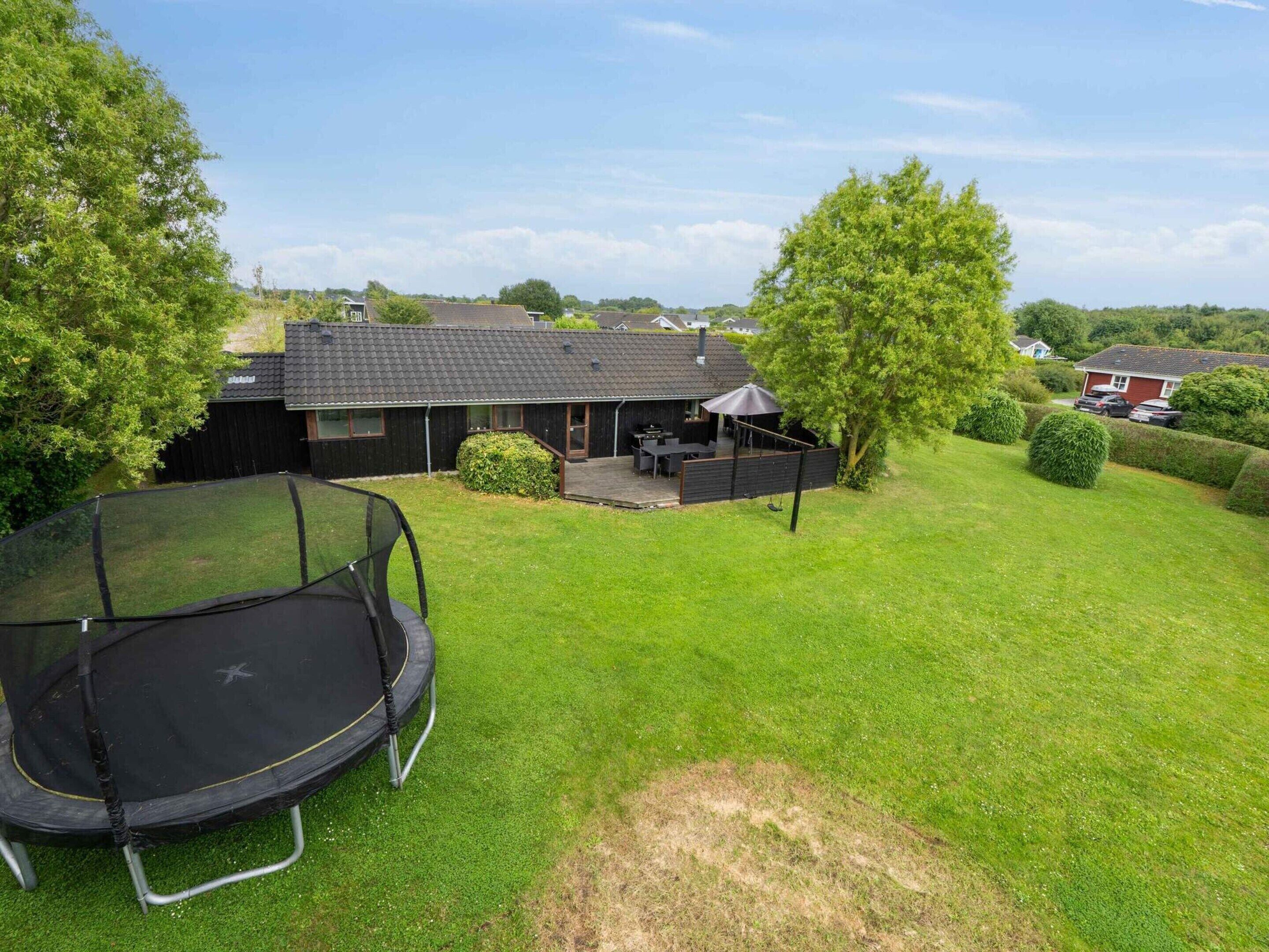A backyard with a trampoline, a patio area with outdoor furniture, and a house with a dark roof.