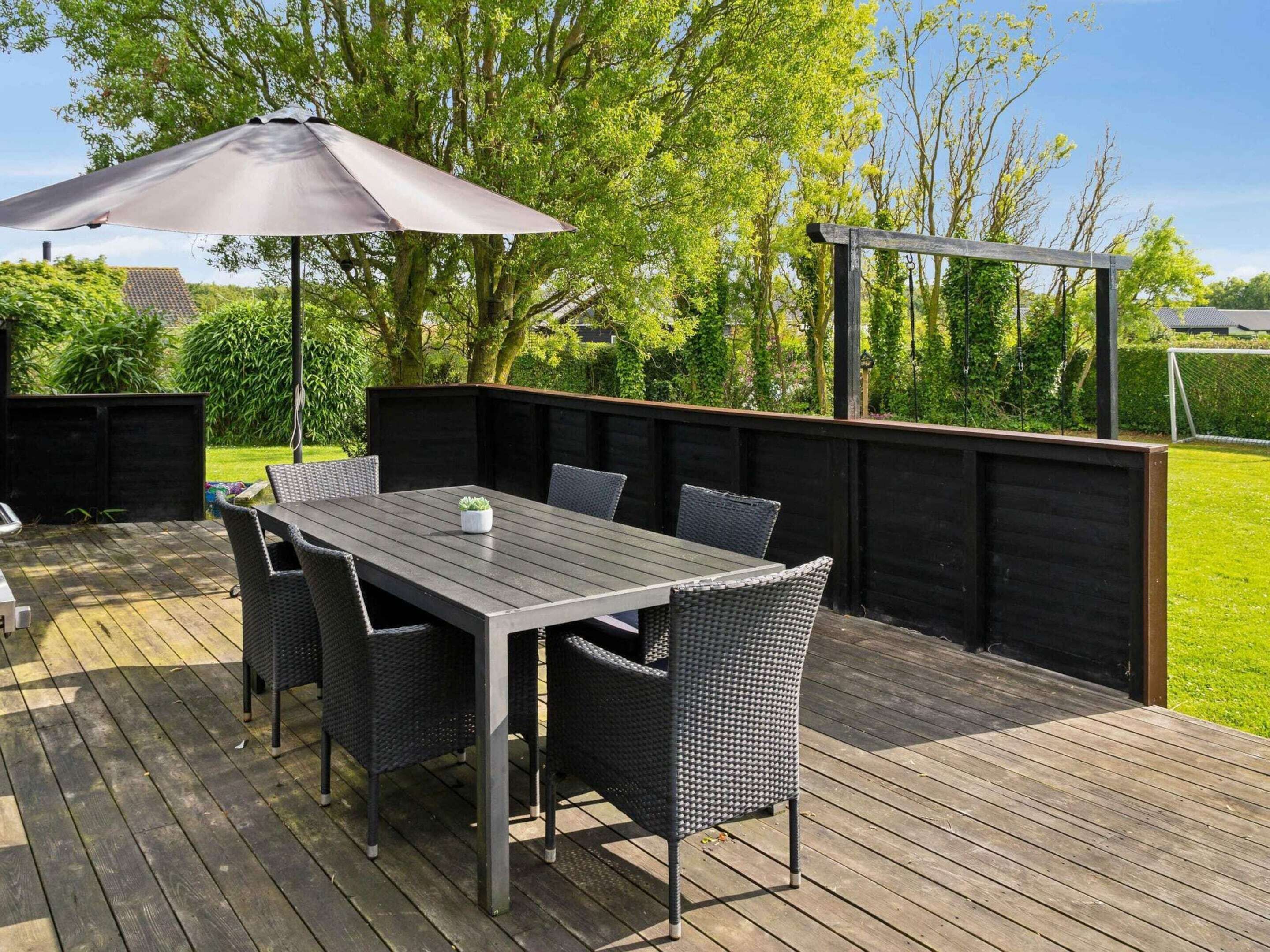 Een terras buiten met een houten terras, een tafel met stoelen en een grote parasol.