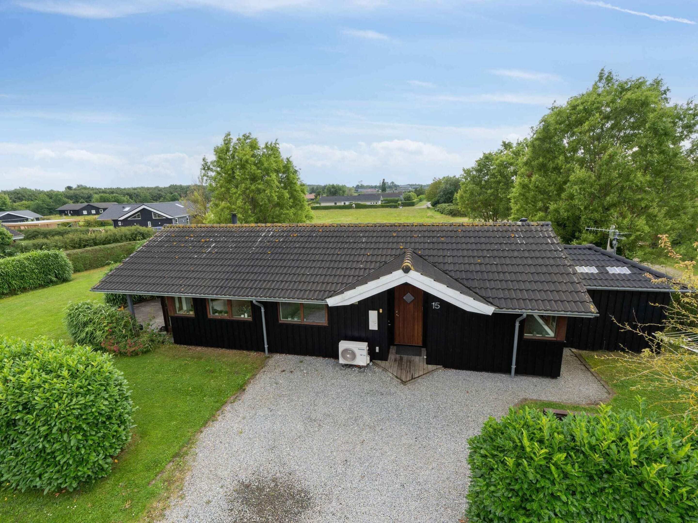 Een zwart huis met een grindpad, omringd door groen en andere huizen op de achtergrond.