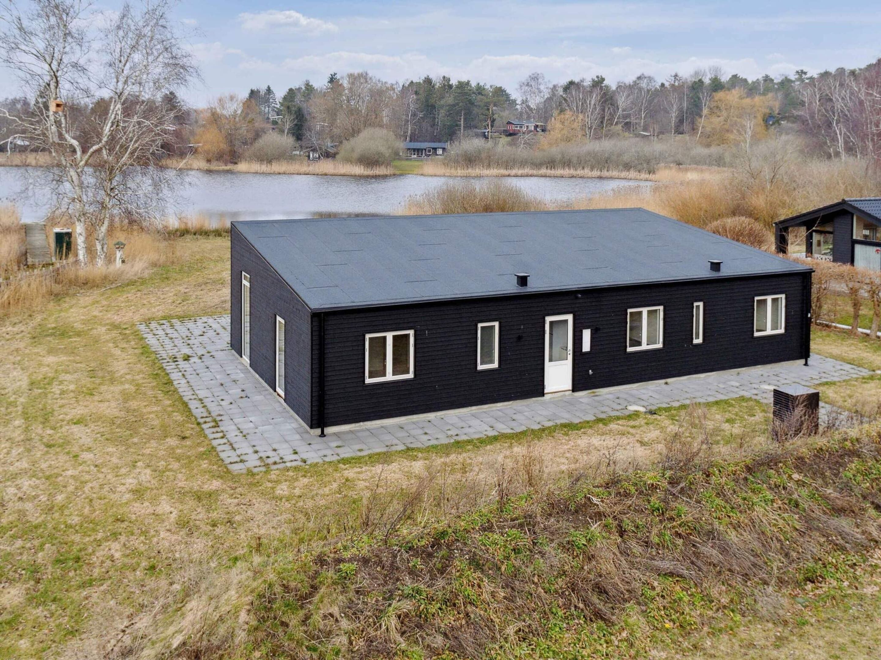 A modern black building with a flat roof, rectangular windows, and a door. It is situated on a grassy area with a paved walkway leading to it.