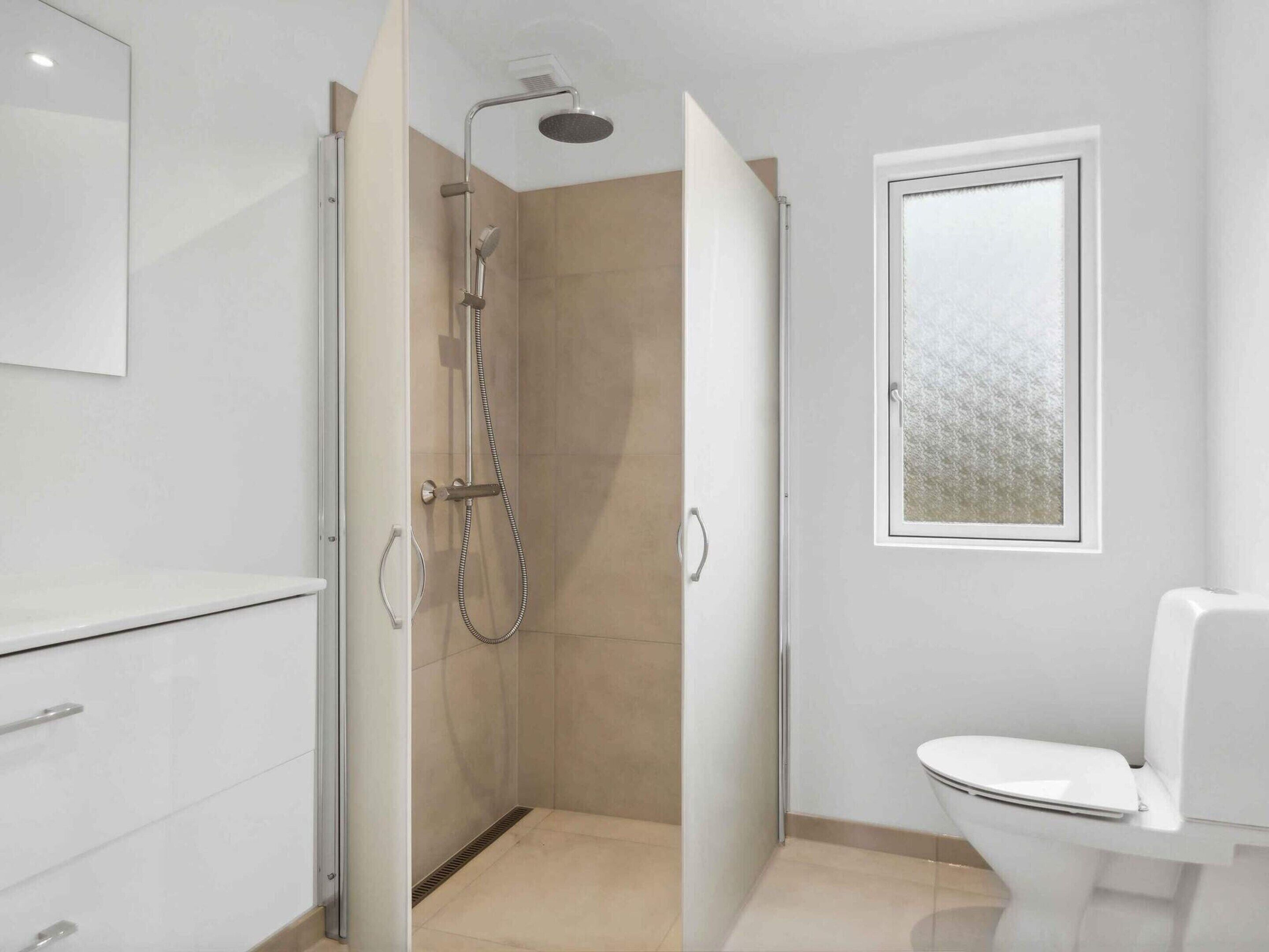 Une salle de bain moderne équipée d’une douche, de toilettes et d’une fenêtre.