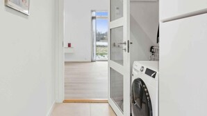 Un espace buanderie comprenant un lave-linge, un étendoir et une porte donnant sur un balcon.