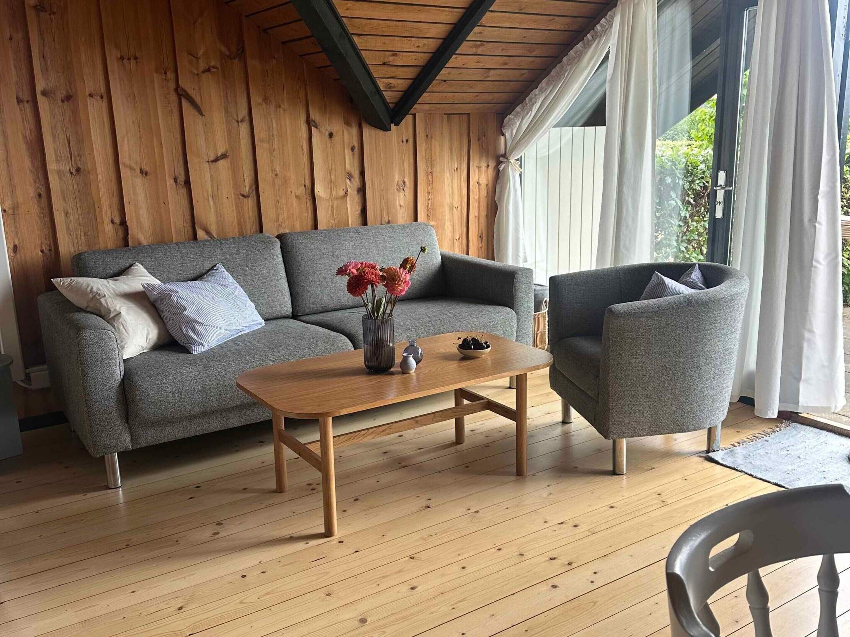 Un salon chaleureux avec un canapé gris, un fauteuil assorti et une table basse en bois.