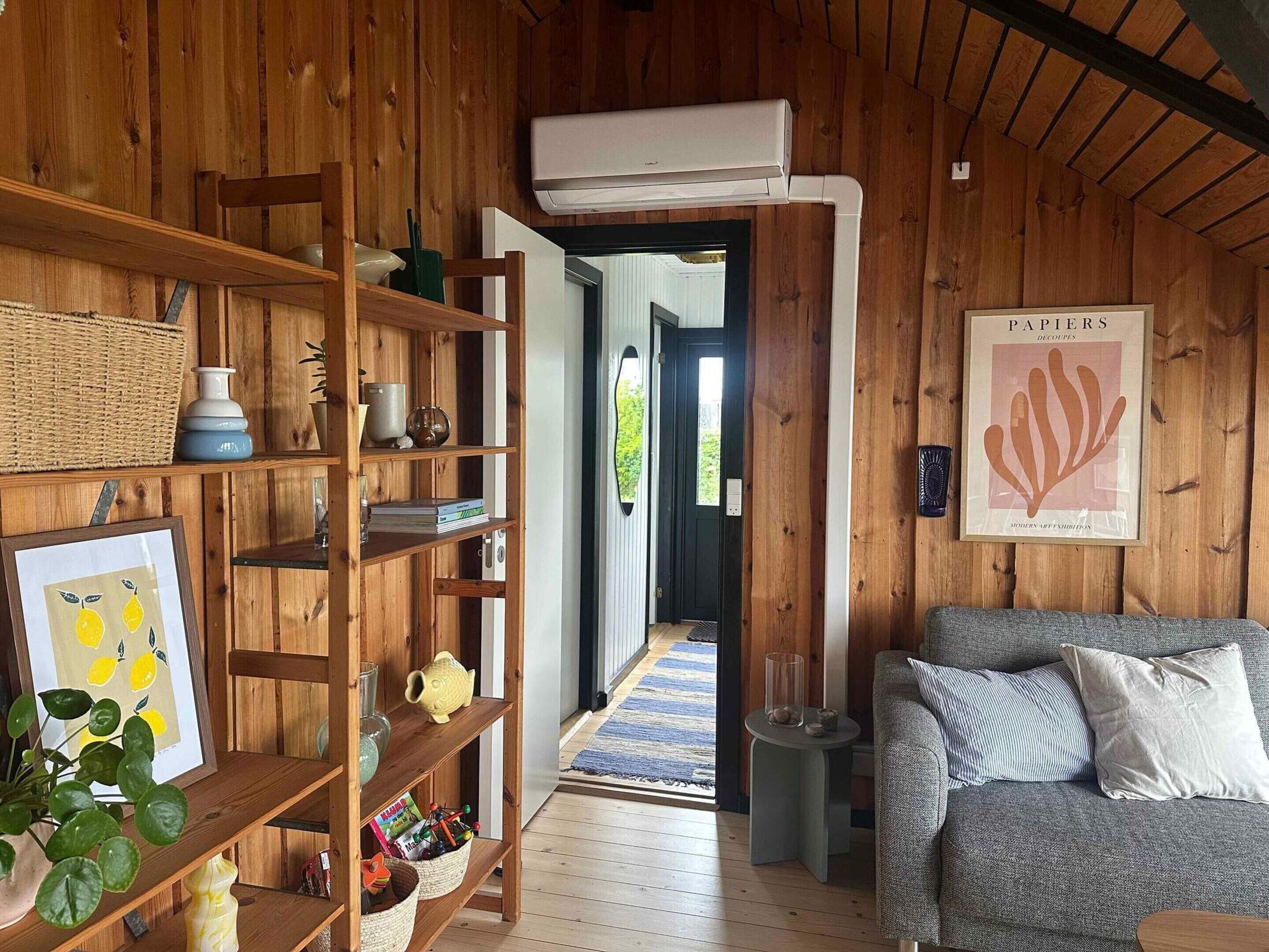 A wooden interior with a bookshelf, a grey sofa, and a framed artwork on the wall.