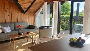 Ein gemütliches Zimmer mit Holzbalkendecke, einem grauen Sofa, einem Holztisch und einem Esstisch mit einer Obstschale.