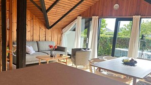 Ein gemütliches Zimmer mit Holzbalkendecke, einer Couch, einem Esstisch und Blick auf Grünfläche.