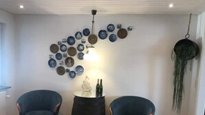 A room with two blue armchairs, a round table with a bottle and a glass, and a wall decorated with various plates and a hanging plant. - 5 Star Holiday Home in Farso (Farso)