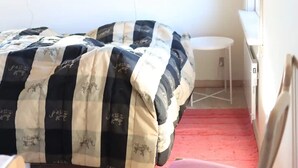 Ein Schlafzimmer mit einem Bett, das mit einer gestreiften Decke bezogen ist, einem kleinen runden Tisch und einem roten Teppich.