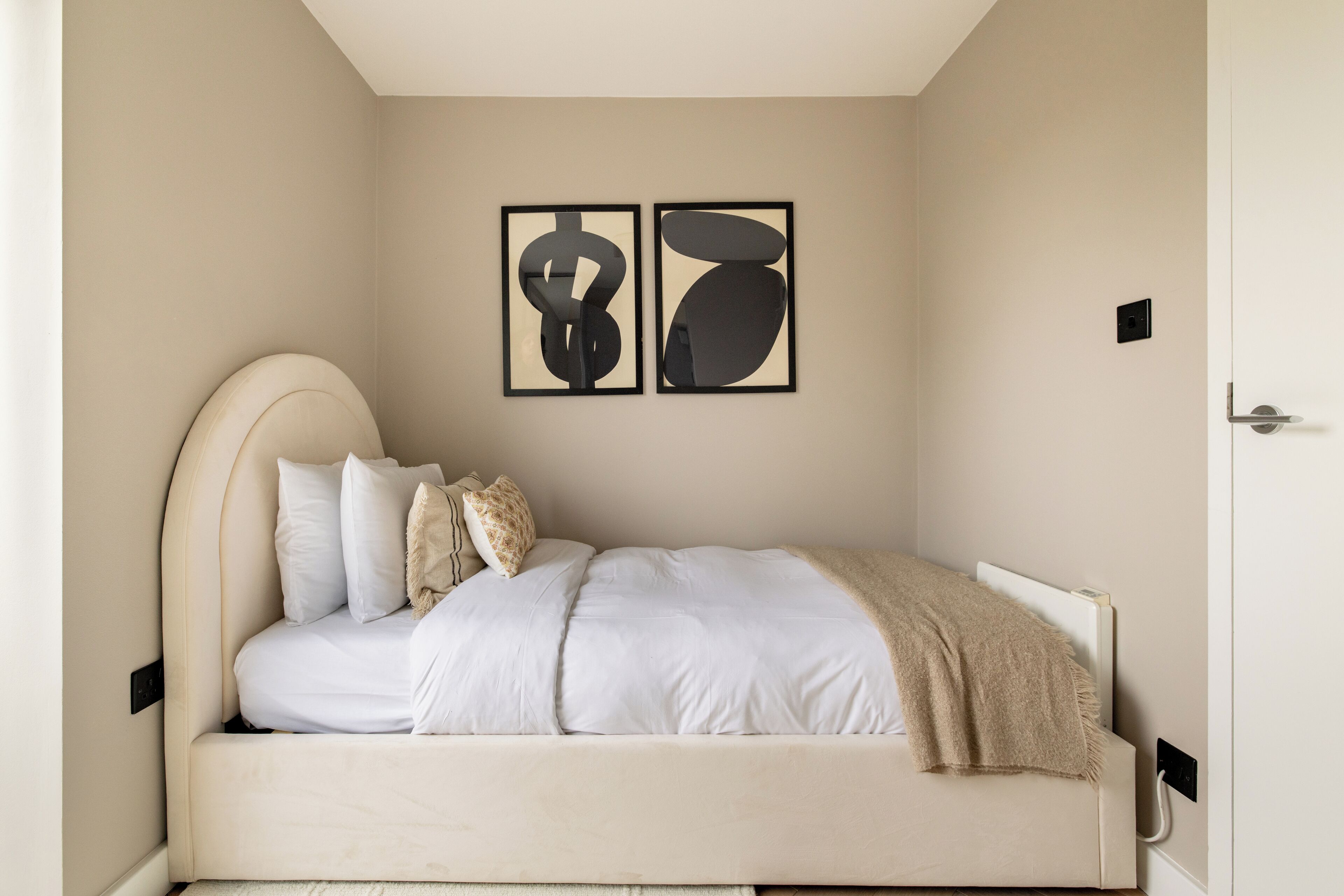A bedroom with a bed, pillows, a blanket, and two abstract wall art pieces.