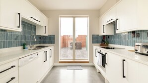 Una cucina moderna con mobili bianchi, lavastoviglie, lavello e tostapane. Una porta scorrevole in vetro dà accesso a un'area esterna.