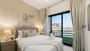 Un dormitorio amplio con una cama grande, una mesita de noche con lámpara y vistas a un edificio a través de un ventanal.