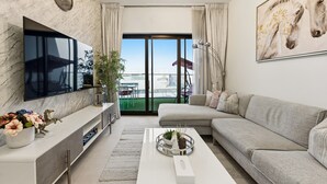 Una sala de estar moderna con televisor de pantalla plana, un sofá gris, una mesa de centro y un balcón con vistas.