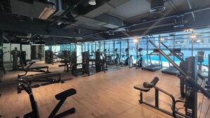 Un gimnasio con diversos equipos de ejercicio, amplias ventanas y suelo de madera.