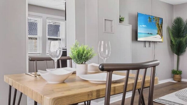 Un coin repas avec une table en bois, des chaises et un téléviseur fixé au mur qui diffuse une scène de plage.