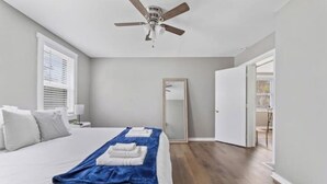 Une chambre à coucher comprenant un lit, un ventilateur de plafond, un miroir et une porte donnant sur une autre pièce.