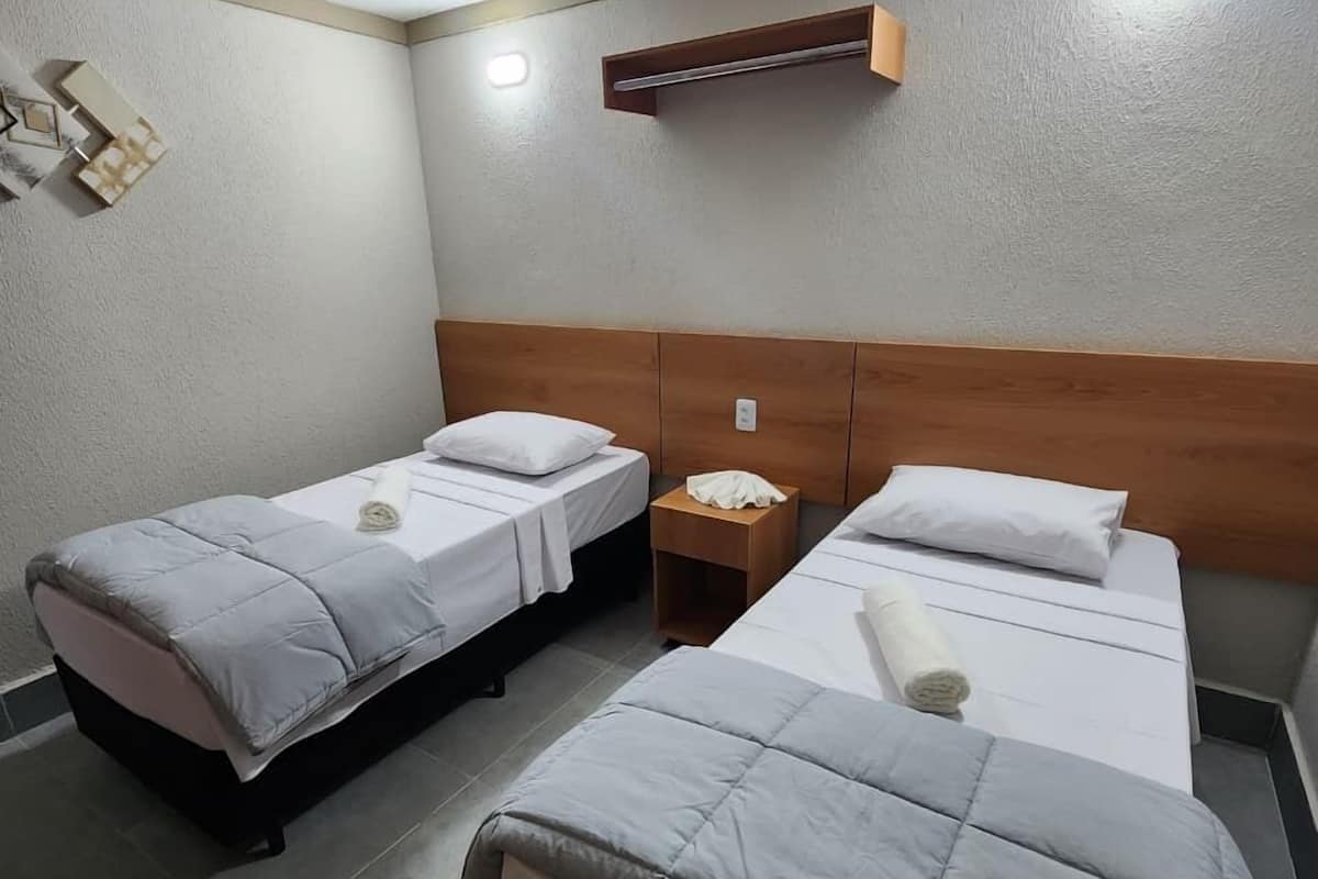 Une chambre d’hôtel avec deux lits simples, une tête de lit en bois, une petite table de chevet et un climatiseur fixé au mur.