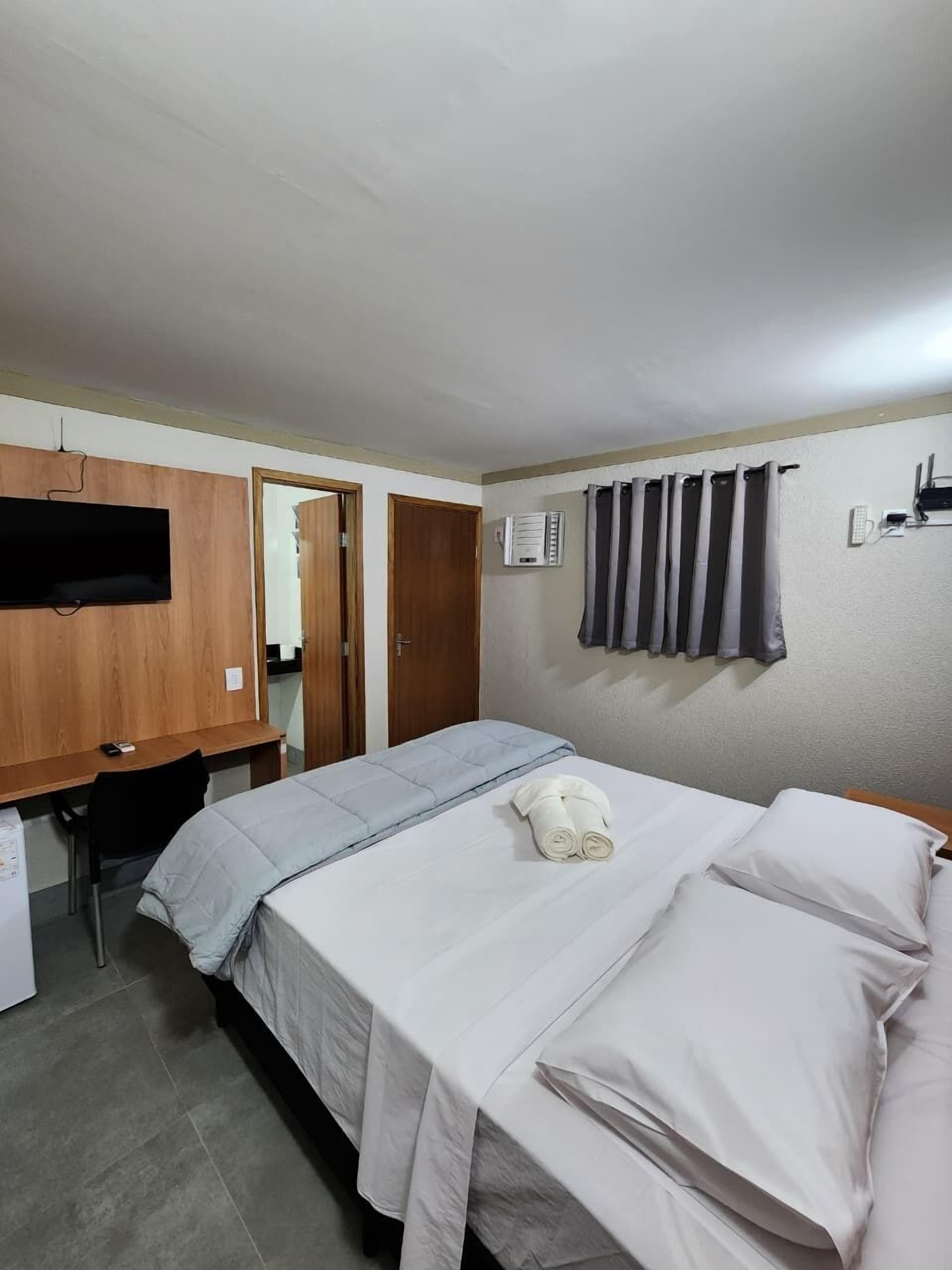 A bedroom with a bed, a desk, a TV, and a shower curtain.