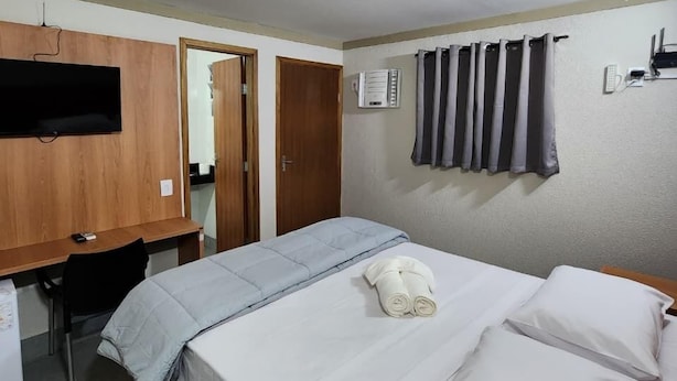 Een slaapkamer met een bed, een bureau, een televisie en een douchegordijn.