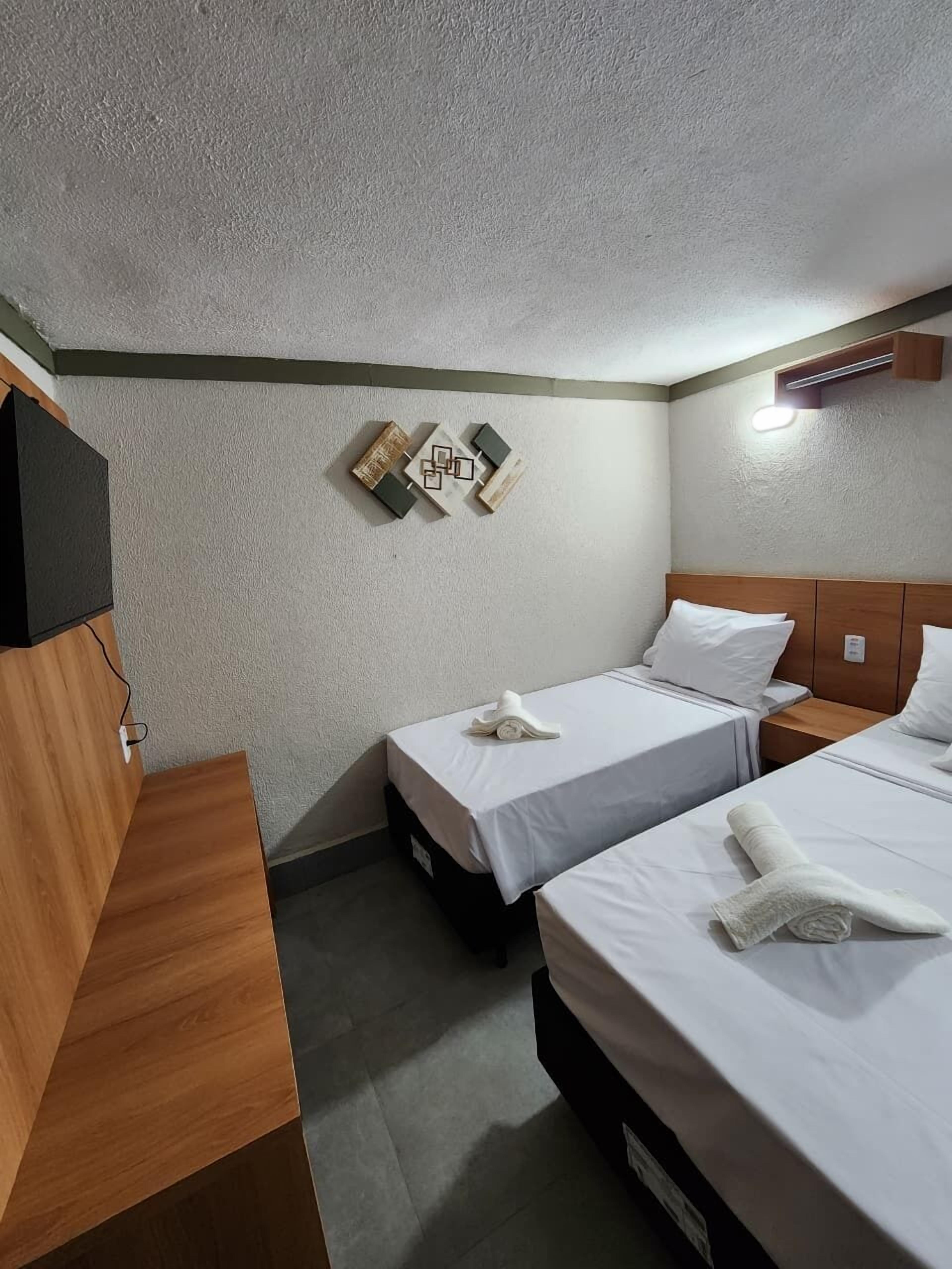 Habitación de hotel con dos camas, un escritorio de madera, un televisor de pantalla plana y una lámpara de pared.