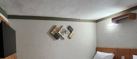 Habitación de hotel con dos camas, un escritorio de madera, un televisor de pantalla plana y una lámpara de pared.