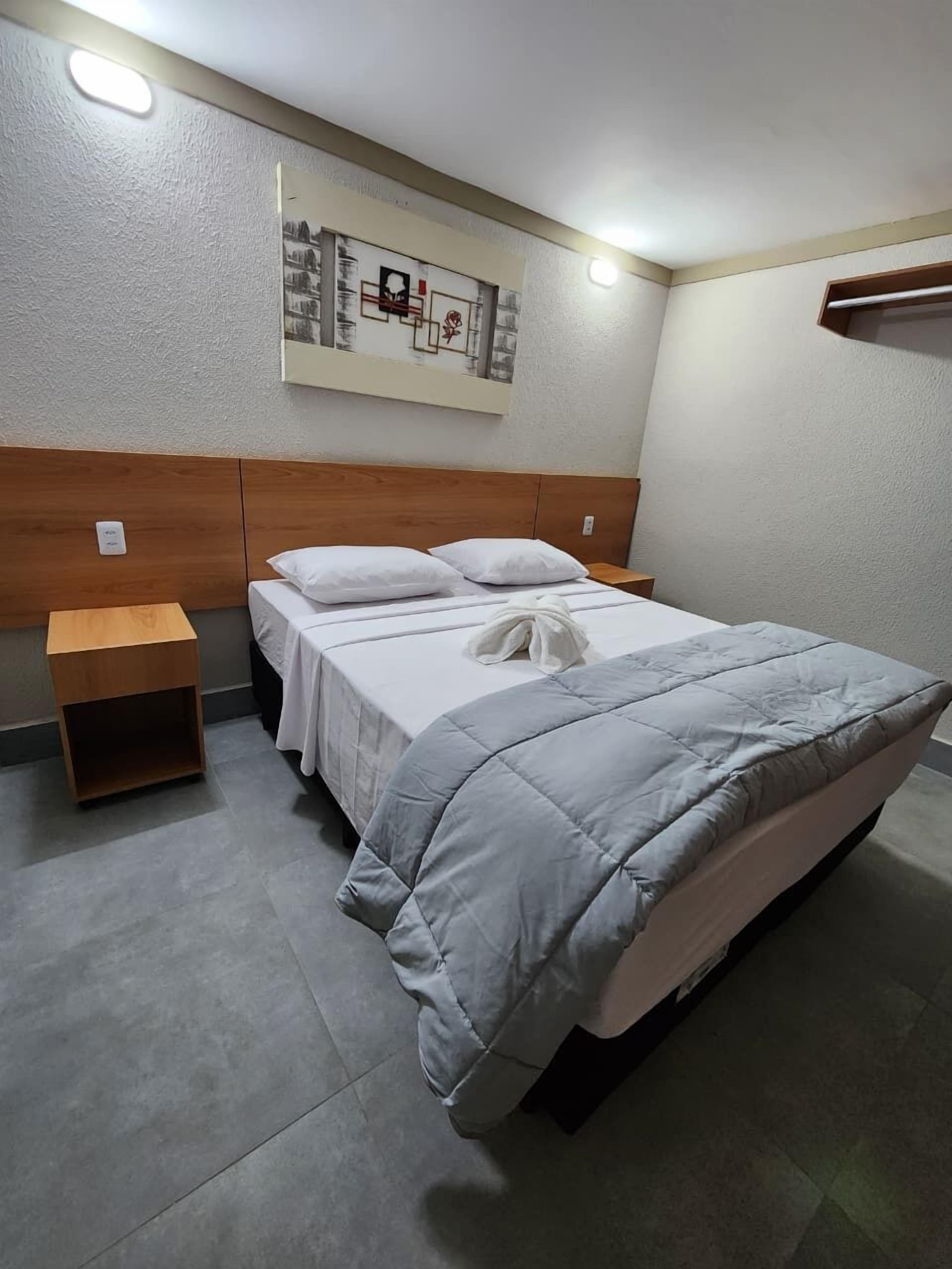 Um quarto bem arrumado com uma cama, duas mesas de cabeceira e uma obra de arte na parede.