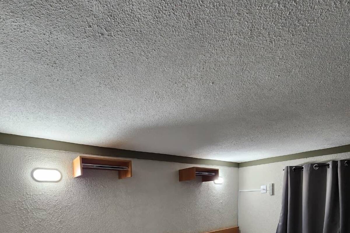 Une chambre d’hôtel avec trois lits simples, une tête de lit en bois, une petite étagère en bois et un luminaire fixé au mur.