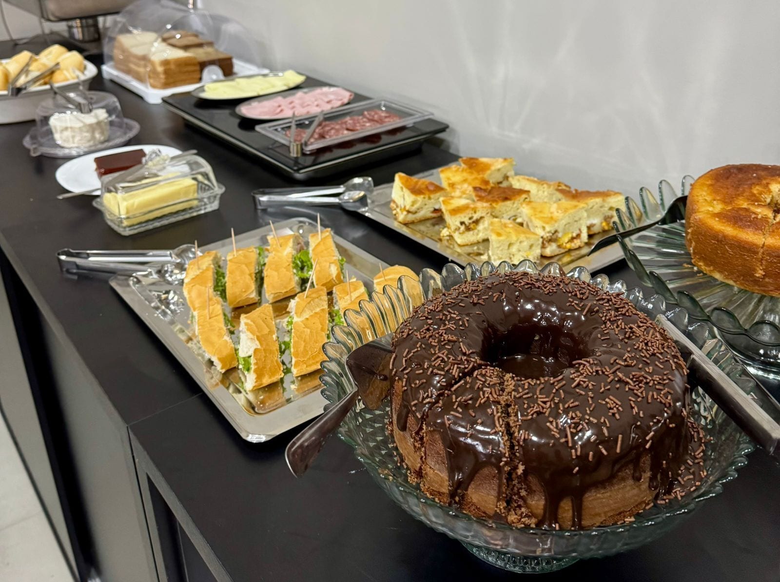 En buffé med olika rätter, inklusive smörgåsar, en chokladtäckt munk och andra desserter.