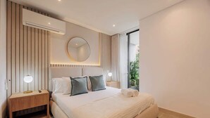 A modern hotel room with a large bed, bedside tables, a round mirror, and a view of greenery outside.